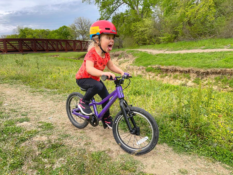 3 year old riding purple Prevelo Alpha Two through field of yellow flowers