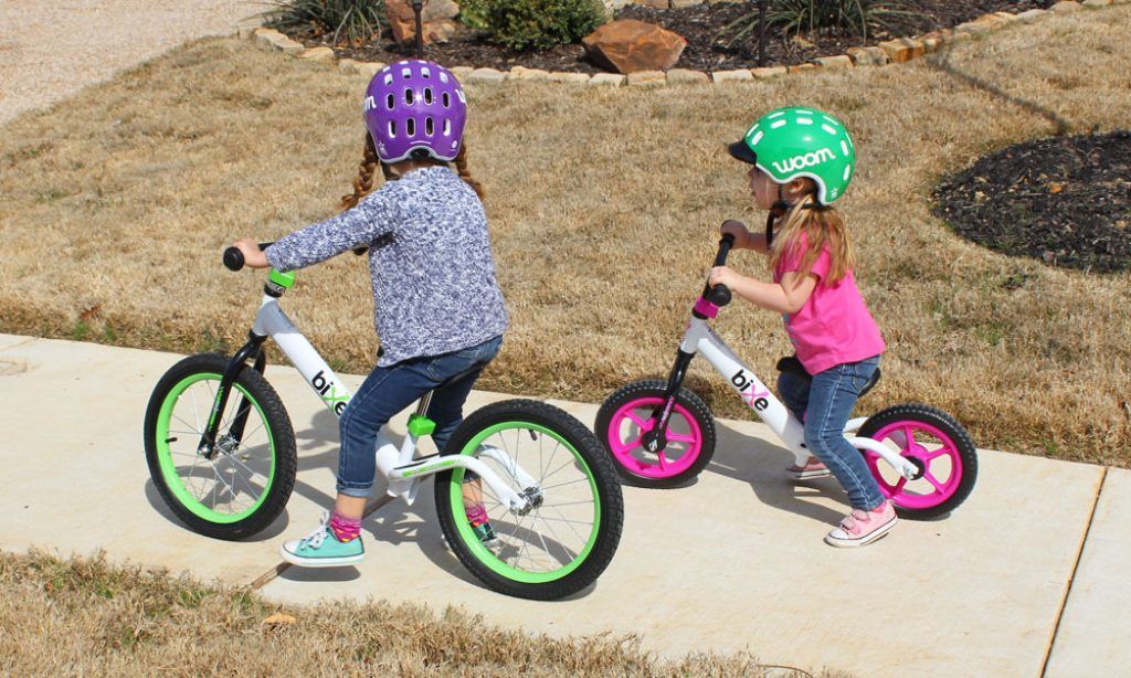 two girls riding a green 16 inch bixe balance bike and a pink 12 bixe balance bike