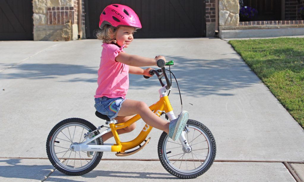 young girl in a pink shirt riding a yellow woom 1 plus balance bike