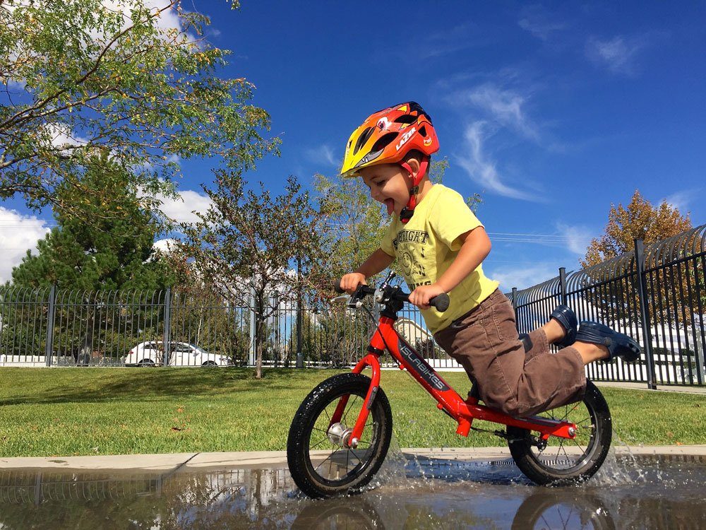 2 year old riding a red balance bike through a puddle