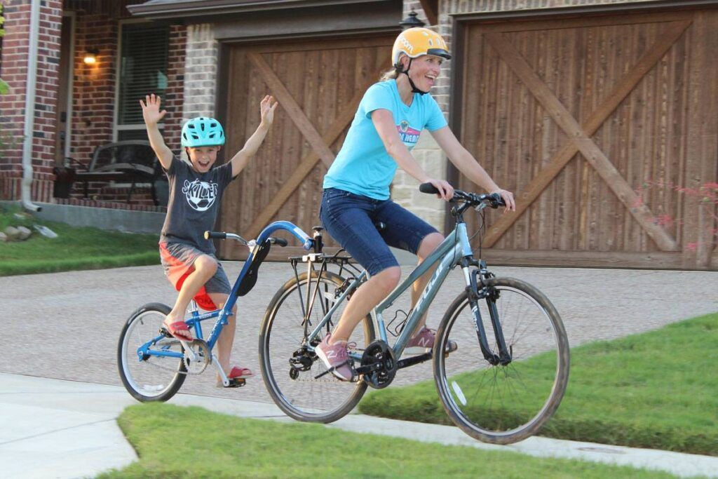 Mom and son riding down the sidewalk on the Burley Kazoo tag along bike