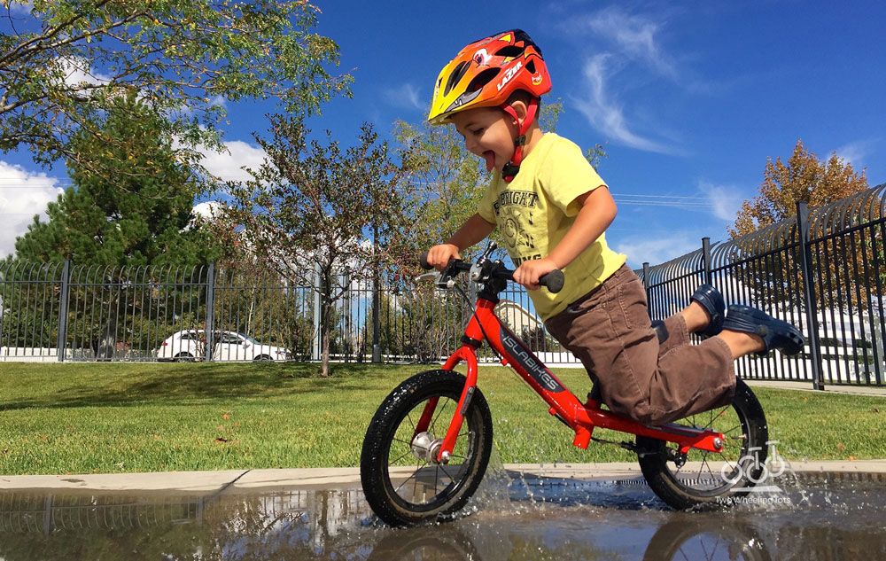 toddler riding a balance bike through a puddle