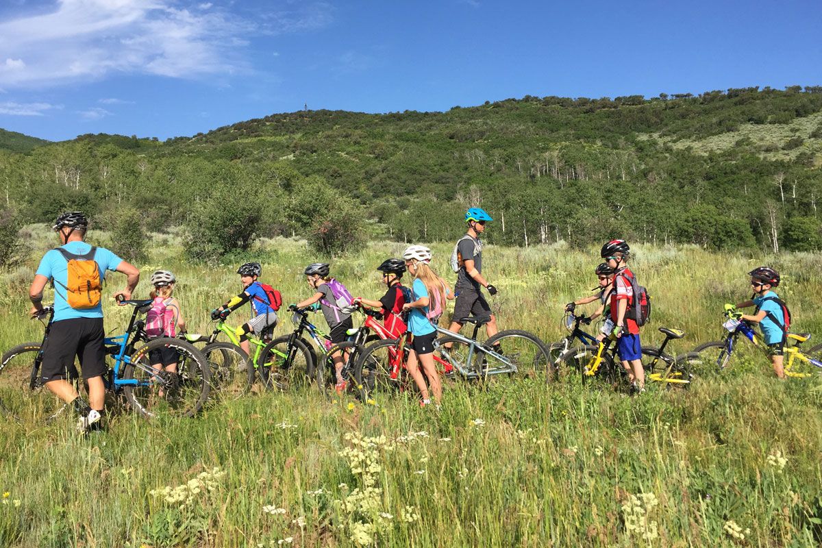 Group of 9 year old kids in a meadow, taking a break during their mountain biking class.