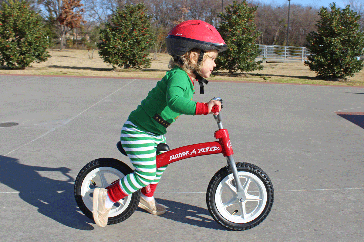 Toddler riding Radio Flyer balance bike at skatepark, leaning in and running.