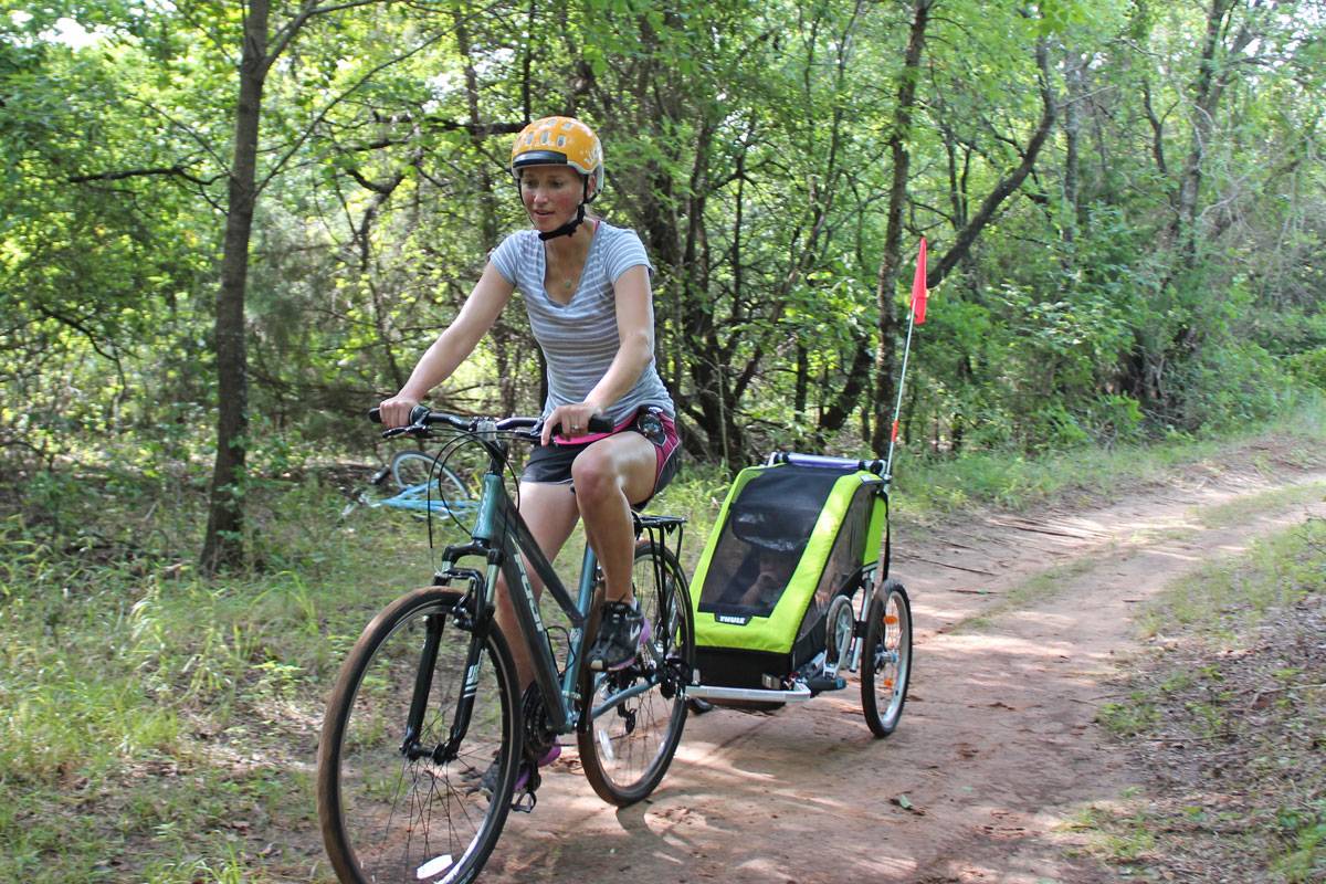 Mom pulling Thule Chariot Cheetah XT single bike trailer on dirt trail in woods