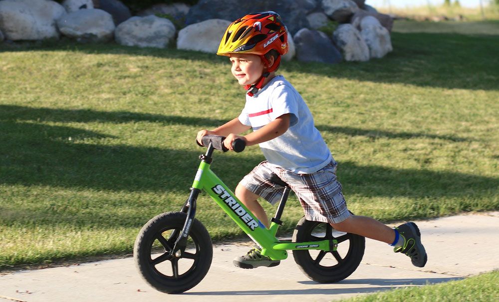 toddler riding a green Strider balance bike