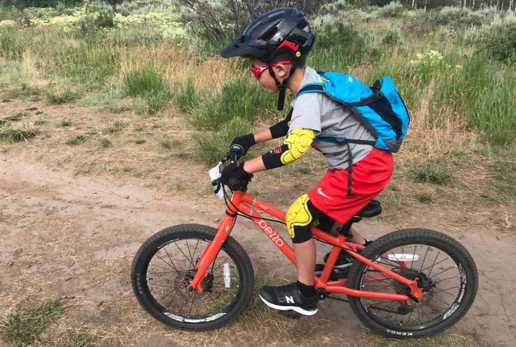 young boy riding his orange bike with a blue camelbak mini mule hydration pack