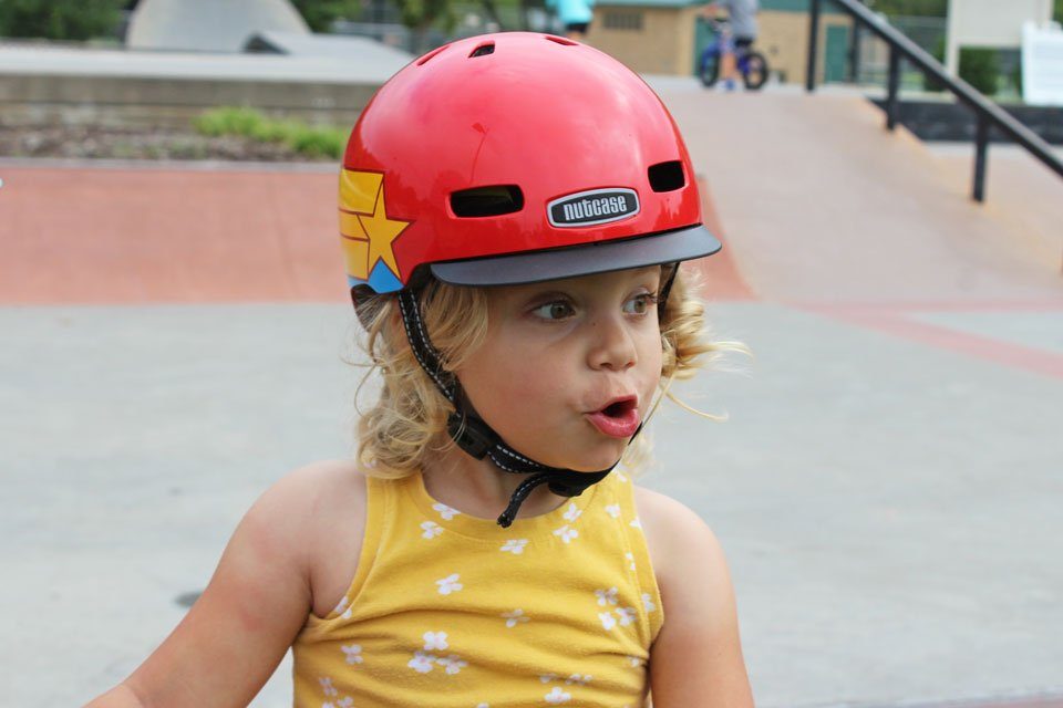 2 year old wearing Nutcase Little Nutty helmet with Wonder Woman pattern. At the skatepark.