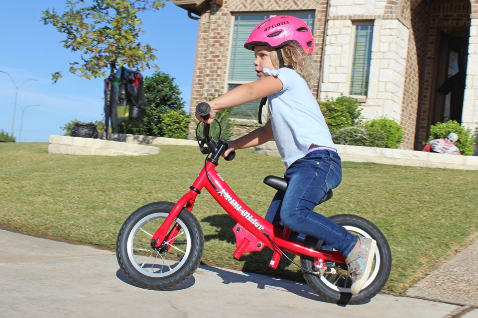 Toddler riding Glide Bikes Mini Glider down a driveway and turning sharply.