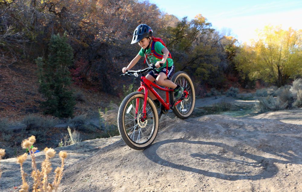 8 year old riding Vitus Plus 24 inch kids bike over dirt roller on mountain bike trail