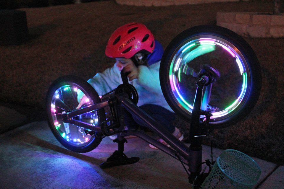 Child inspecting the wheels of her bike that are lit up in the dark with Activ Life bike wheel lights