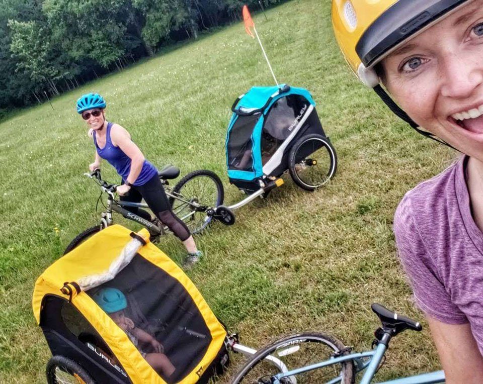 Two moms with their Burley bike trailers. One has a Burley Bee, the other has a Burley D'Lite X.
