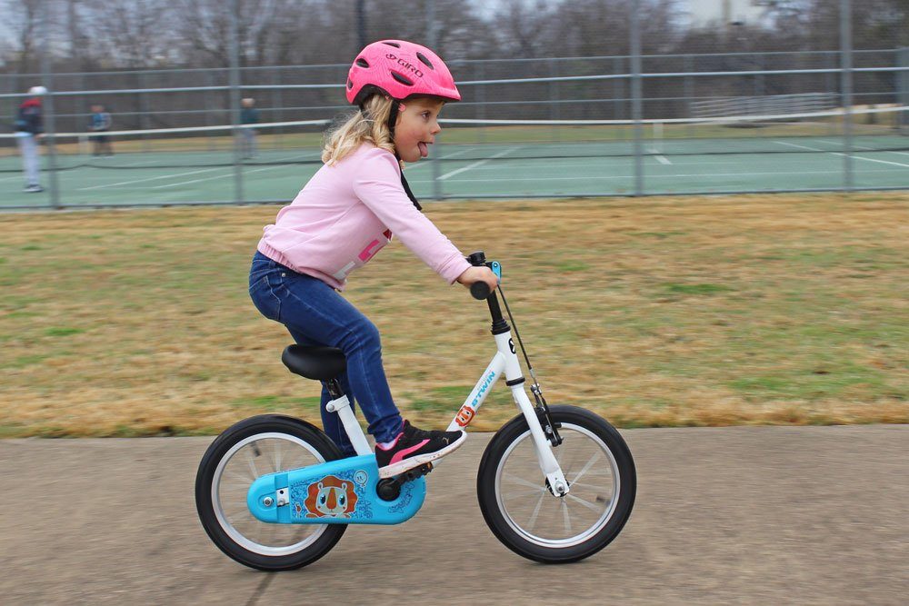 3 year old girl standing up on the pedals while riding the Btwin 14