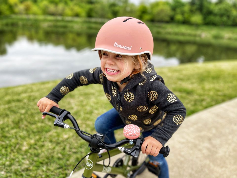 Young child on bike wearing pink Thousand Jr kids bike helmet