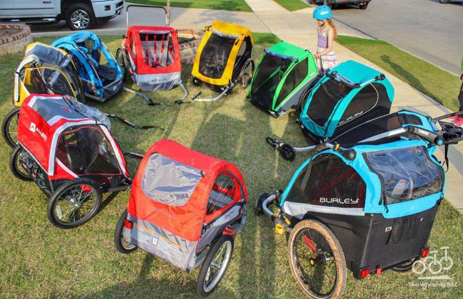 8 different kids bike trailers in a circle for a review, including Thule, Burley, Schwinn inStep and Allen