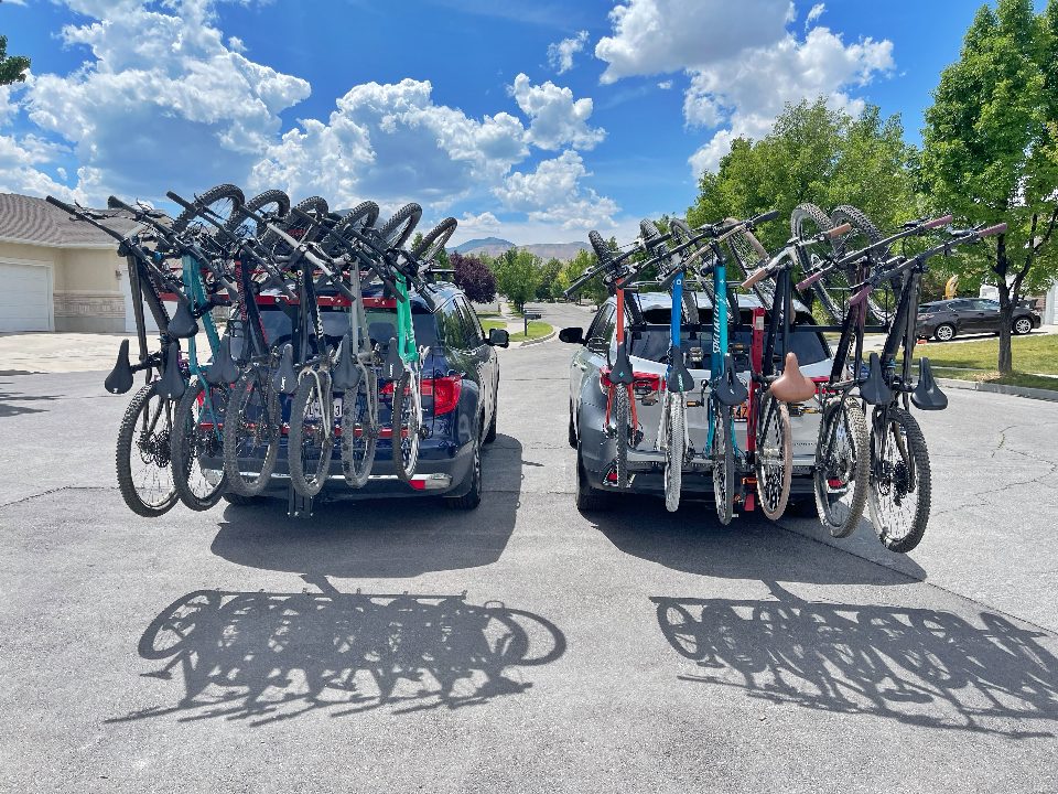 Two cars side by side with Velocirax and Alta Rack vertical bike racks fully loaded. Shown from rear.