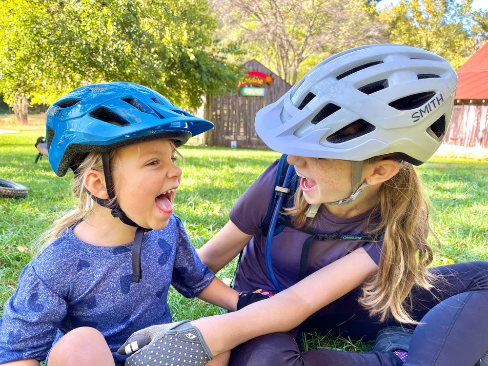 Two girls wearing kids bike helmets while taking a rest on the grass