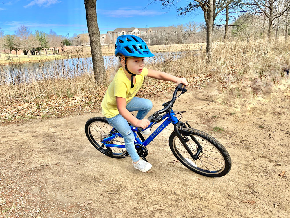 Young girl riding Prevelo Alpha Three 20 inch bike on a dirt trail. Leaning through a turn.