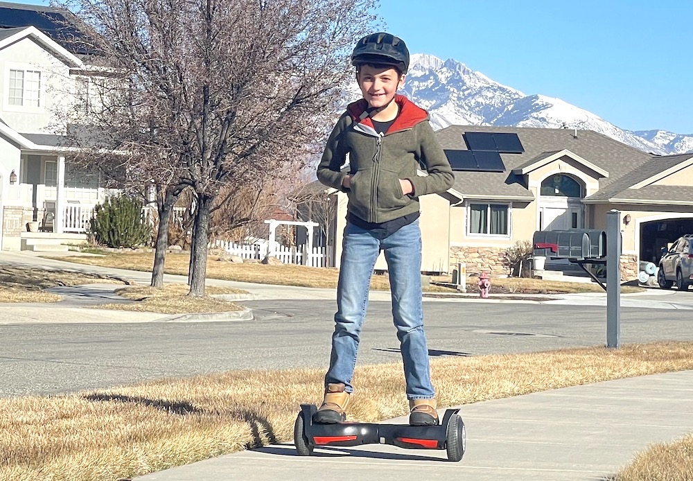 小男孩骑着 Swagtron Twist 悬浮滑板沿着人行道行驶。
