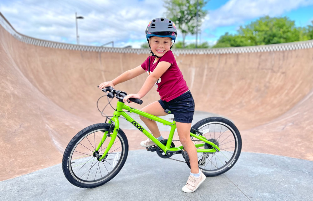 Child smiling while sitting on her Frog 52 bike at the skatepark