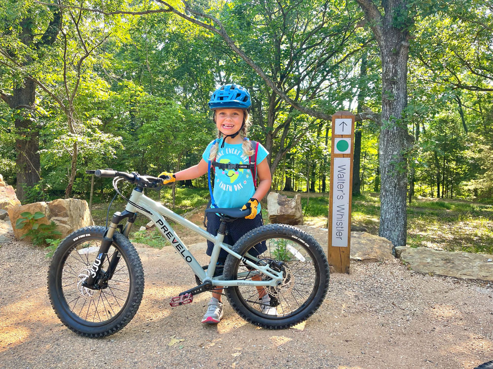 Child standing at the top of a trail with her Prevelo Zulu Three mountain bike