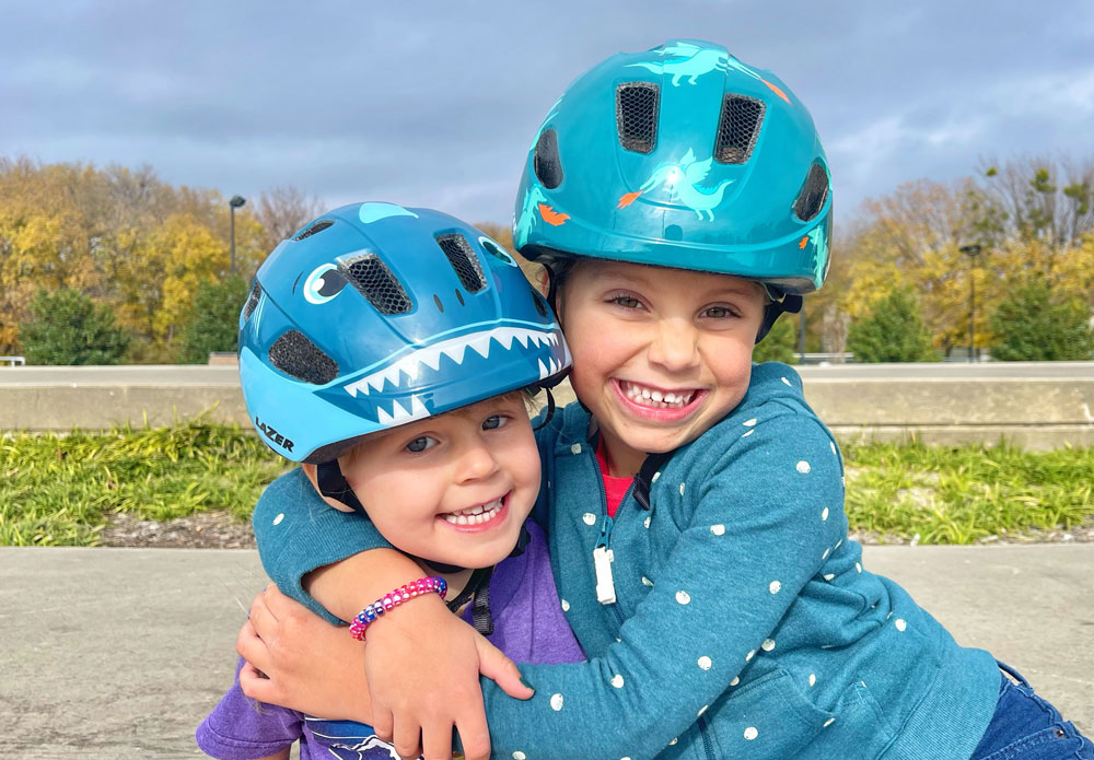 Two kids hugging and wearing Lazer Nutz and Lazer Pnut bike helmets