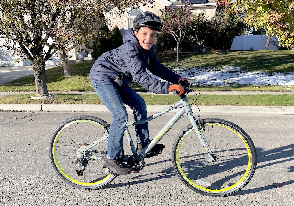 10 year old smiling and riding a gray Guardian 26" kids bike.