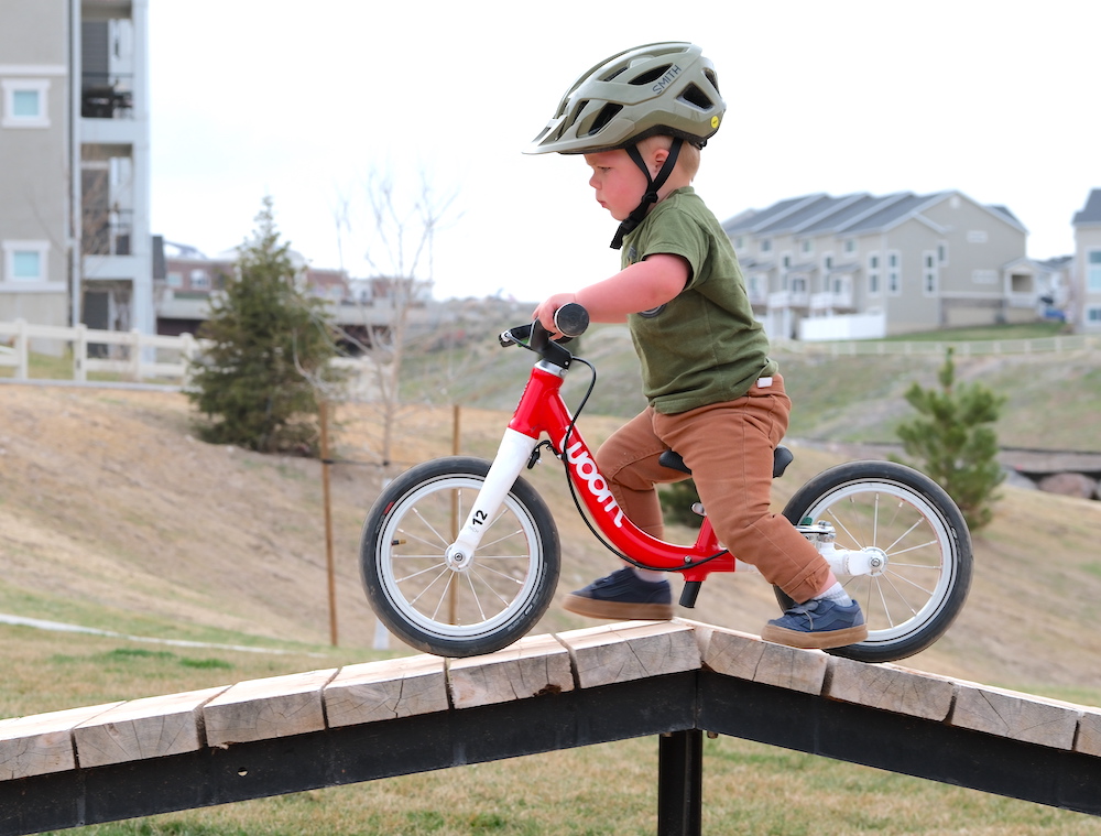 toddler riding the woom 1 over a wooden feature at a bike park