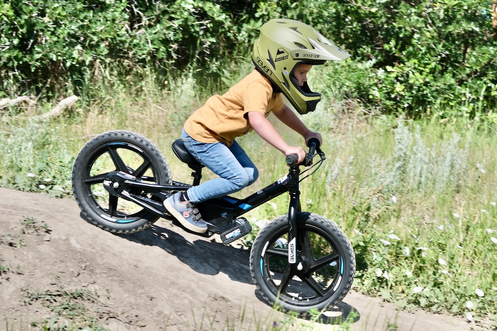 young boy riding a stacyc electric balance bike down a hill