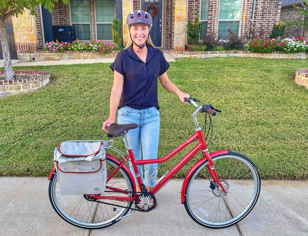 Woman standing next to Priority Turi bicycle in red, with 174Hudson pannier tote attached.