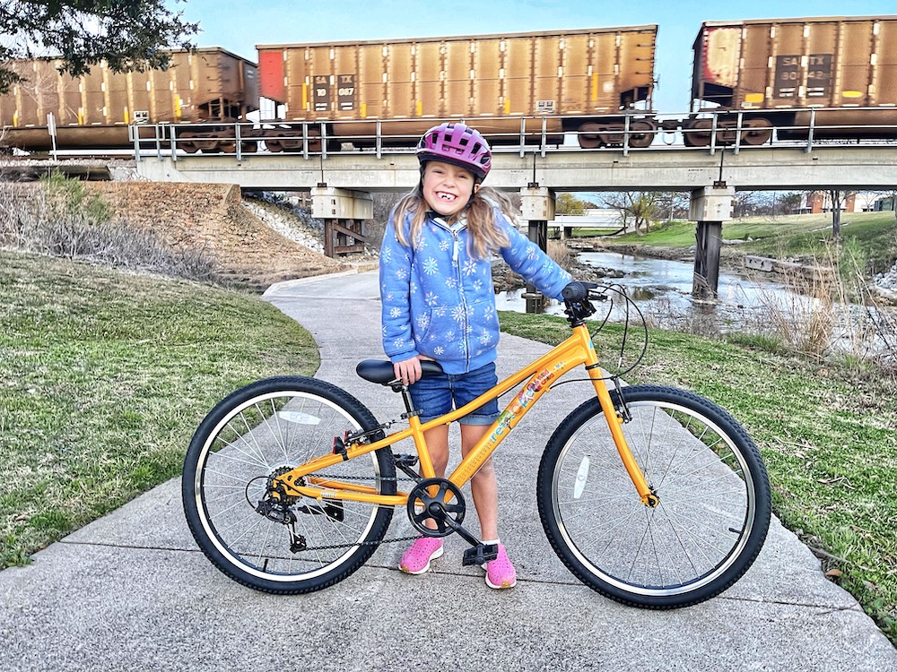 6 year old rider standing with her Retrospec Dart 24 bike